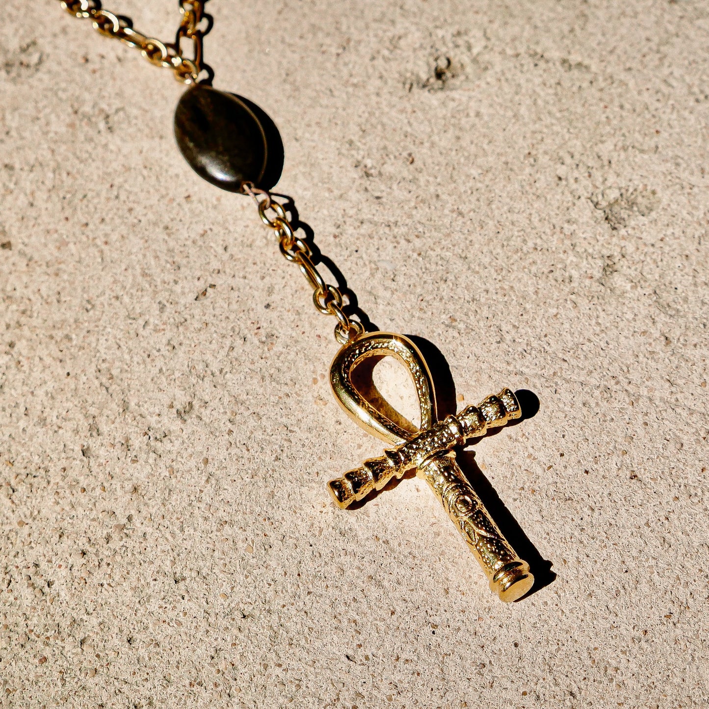 Gold Ankh pendant necklace on a textured beige surface