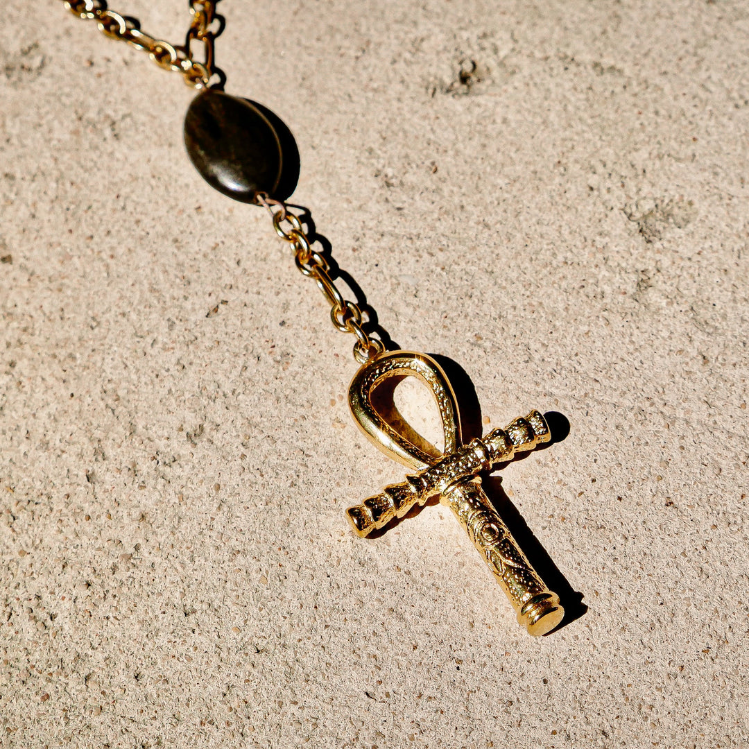 Gold Ankh pendant necklace on a textured beige surface